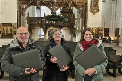Ein Mann und zwei Frauen stehen in einer Kirch und halten graue Sitzkissen in den Händen - Copyright: Annkathrin Bornholdt