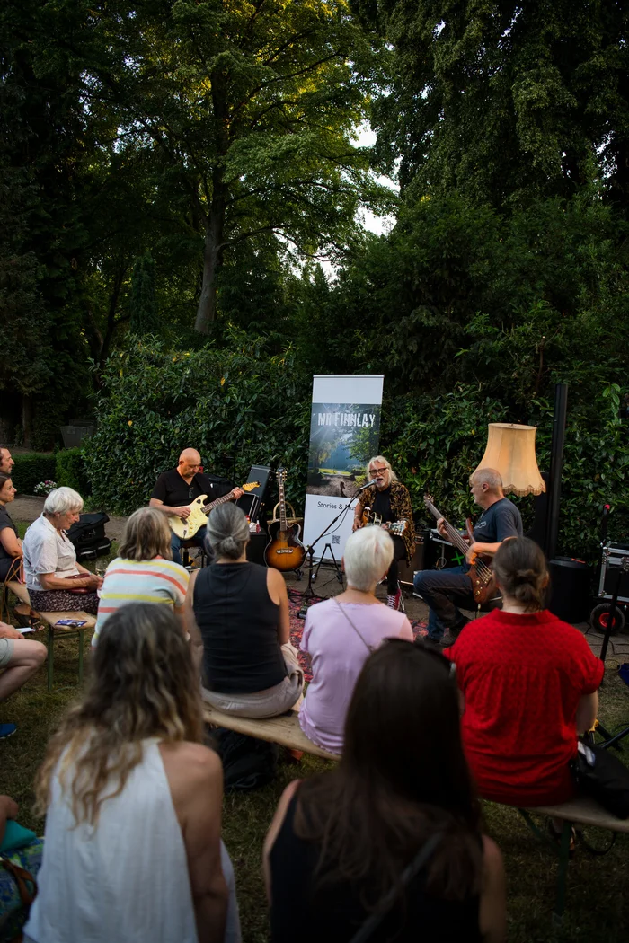 Menschen sitzen im Grünen und hören einem Konzert zu. 