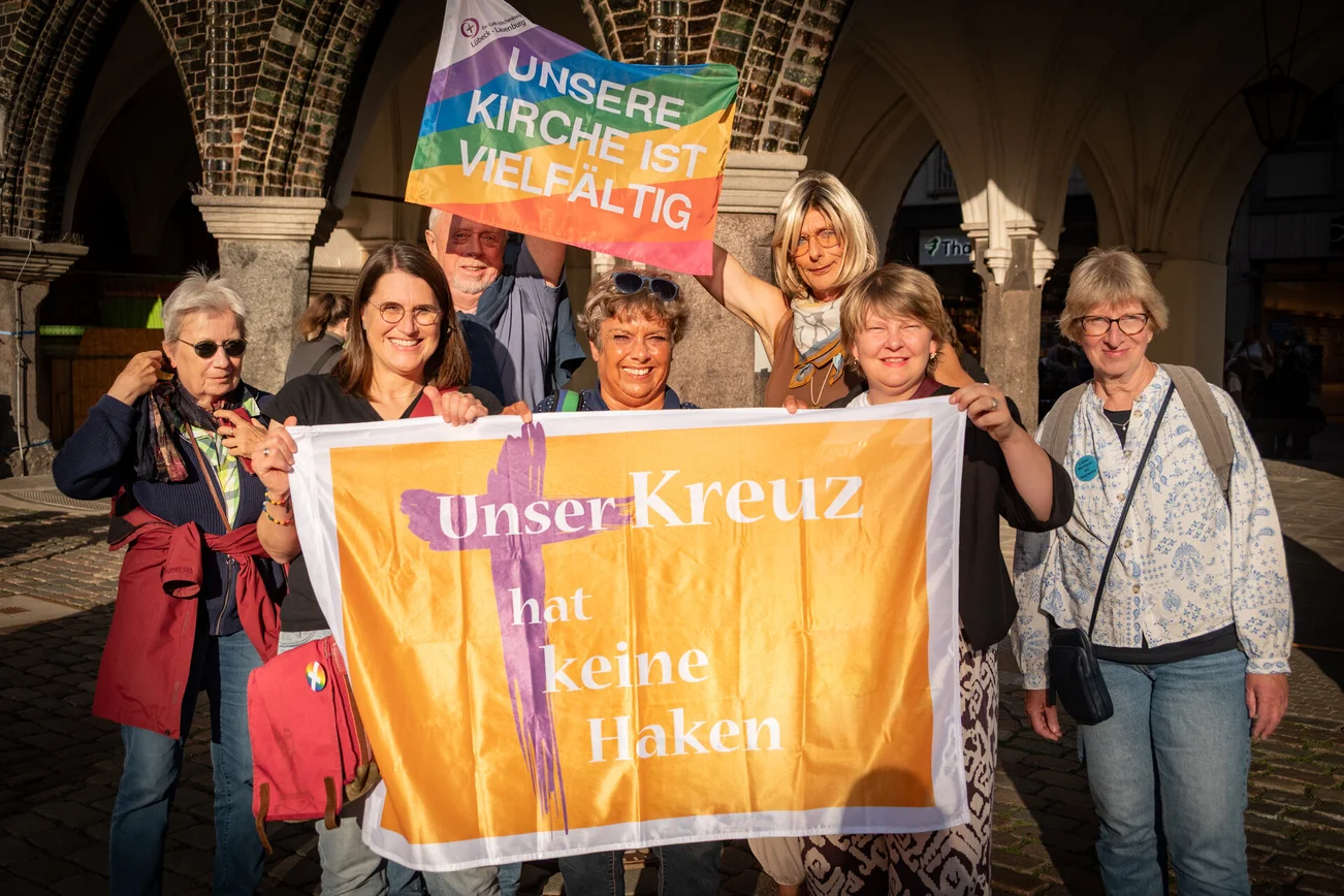 Gruppe von lächelnden Menschen hält zwei bunte Fahnen