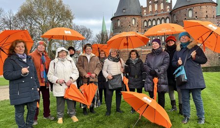 Eine Gruppe von Frauen steht mit orangenen Schirmen vor dem Holstentor. 