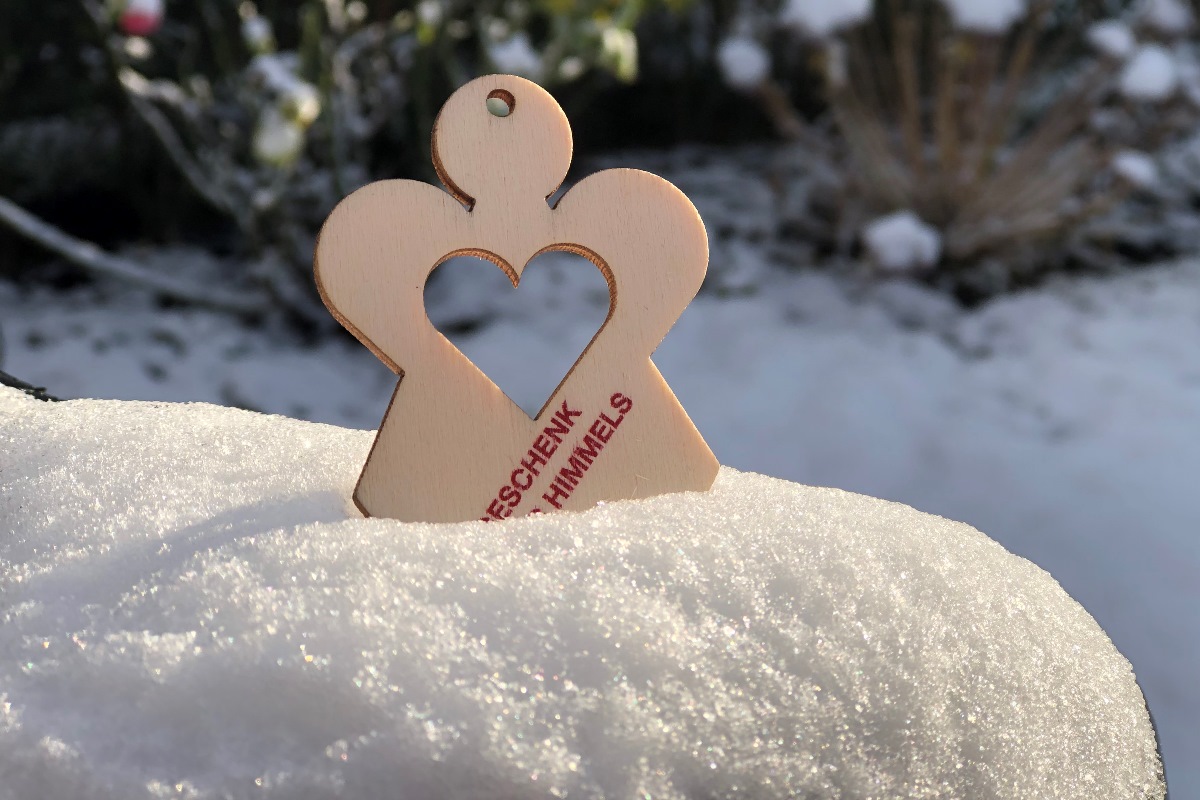 Ein Holzengel mit Herz und Aufschrift Geschenk des Himmels steckt im Schnee