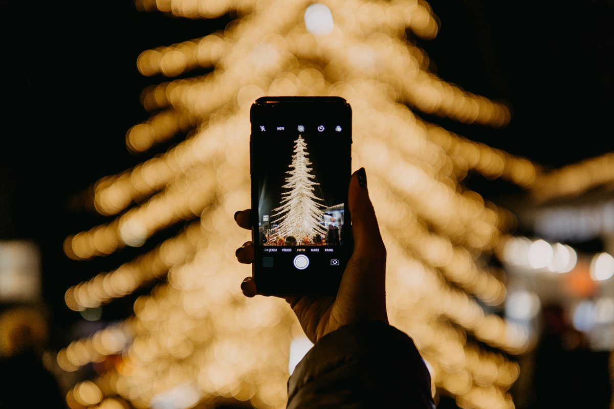 Eine Person hält ein Smartphone vor einen Weihnachtsbaum und fotografiert diesen. 