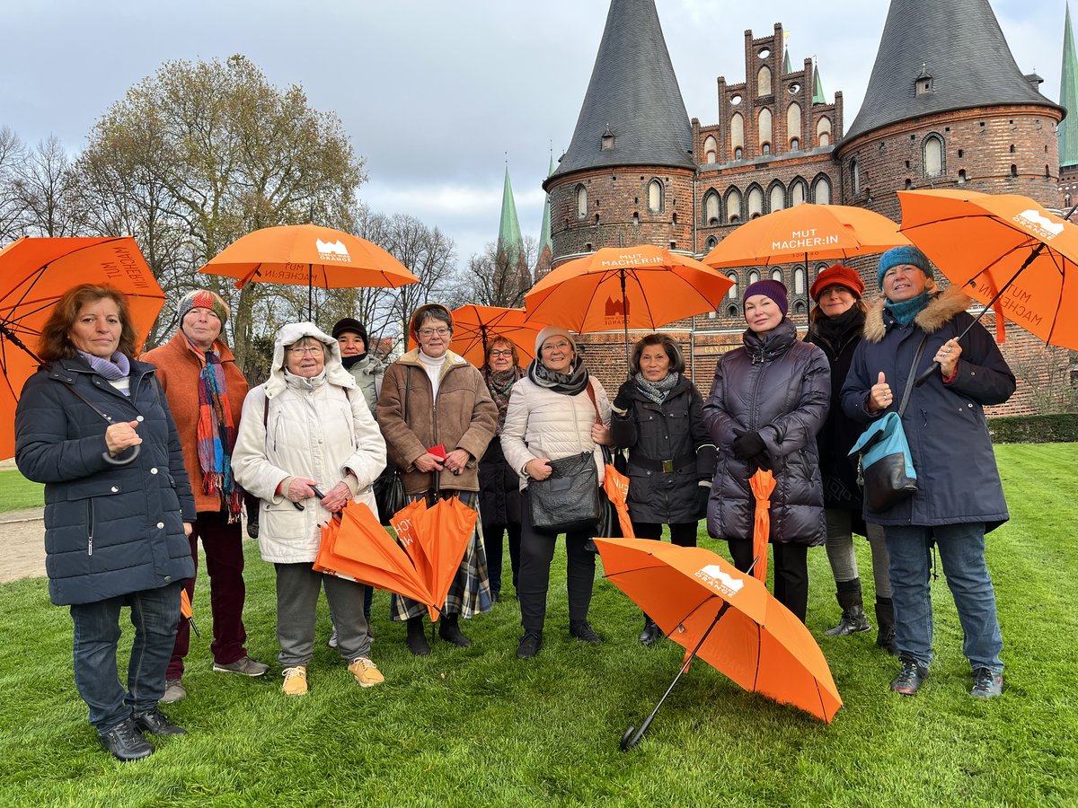 Eine Gruppe von Frauen steht mit orangenen Schirmen vor dem Holstentor. 