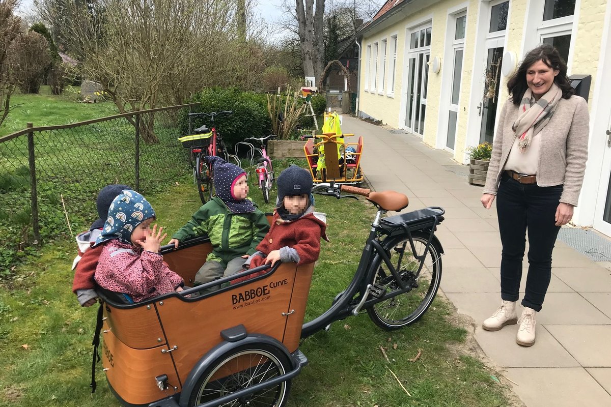 Eine Frau steht neben einem Lastenrad mit mehreren Kindern