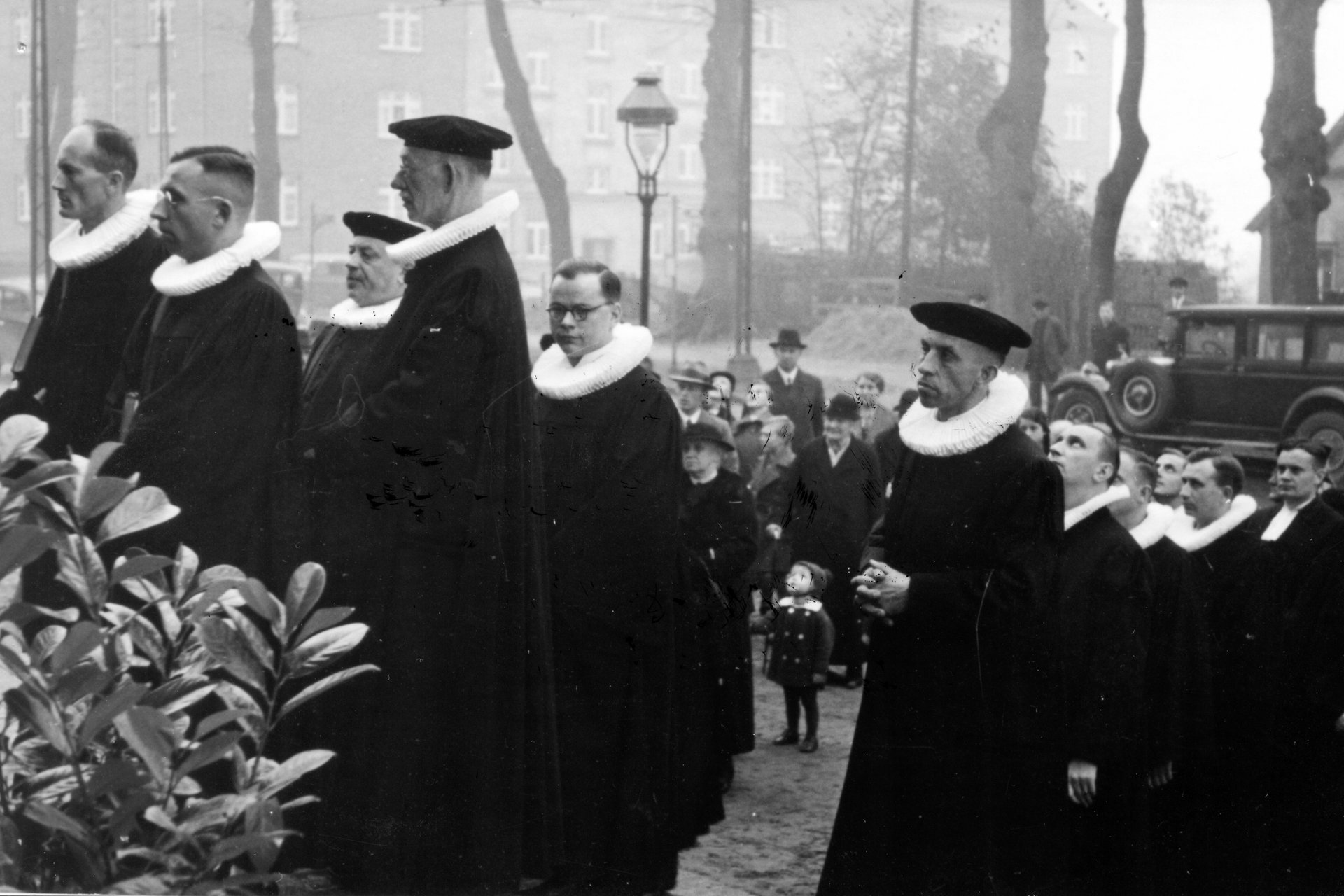 Schwarzweiß Aufnahme von mehreren Pastorn in Ornat, die in eine Kirche einziehen.