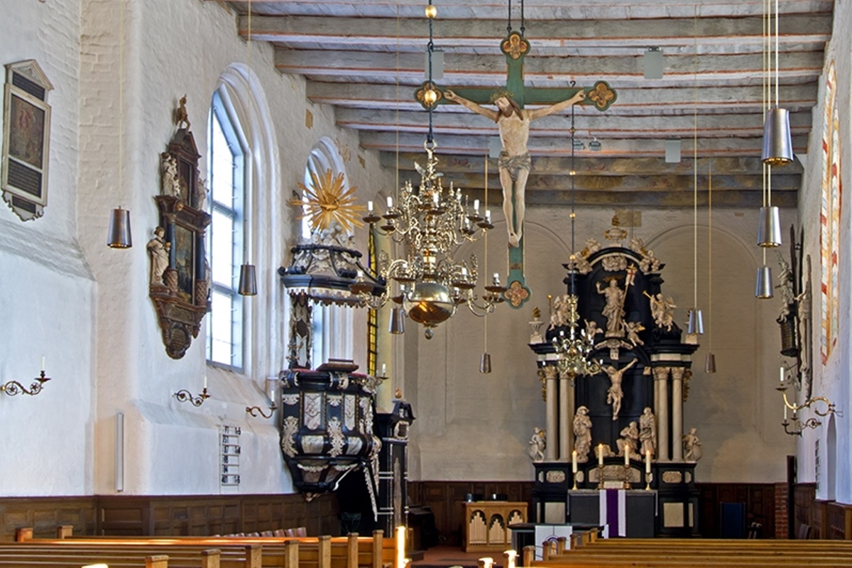 Der Innenraum einer Kirche mit Bänken, einer Kanzel und einem Altar. Ein Kreuz hängt im Raum.
