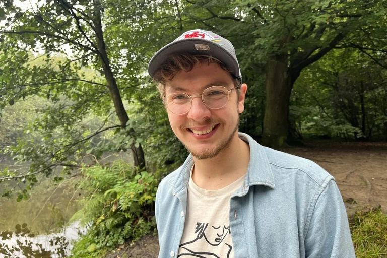 Ein junger Mann mit Brille und Basecap lächelt in die Kamera.