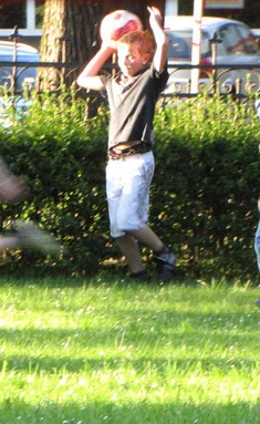 Vier Jungen spielen auf einem Rasen der Teils sonnenbeschienen ist. Der zweite Junge von links hält einen Ball über seinem Kopf