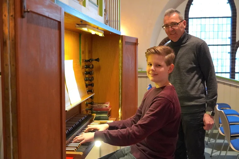 Jugendlicher Schüler auf einer Orgelbank, daneben steht sein Lehrer.