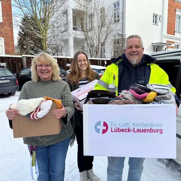 Drei Personen stehen mit Kartons vor einem Auto 