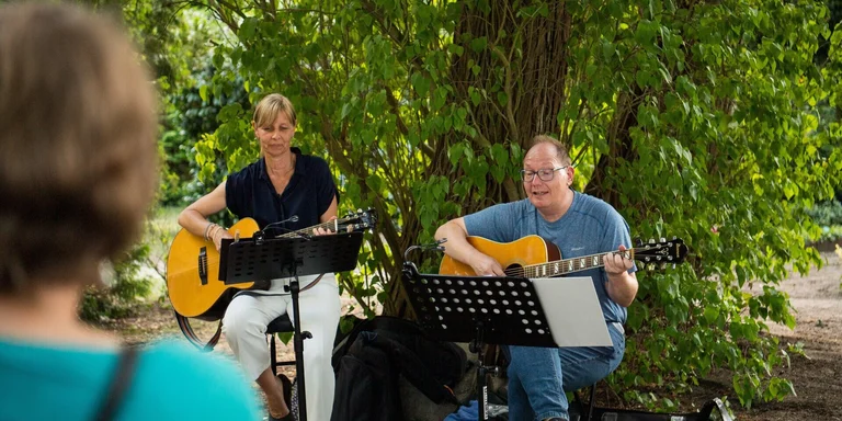 Eine Frau und ein Mann spielen Gitarre und singen im Grünen.