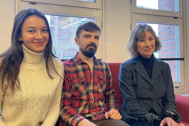 Zwei Frauen und ein Mann sitzen auf einem Sofa und lächeln in die Kamera.