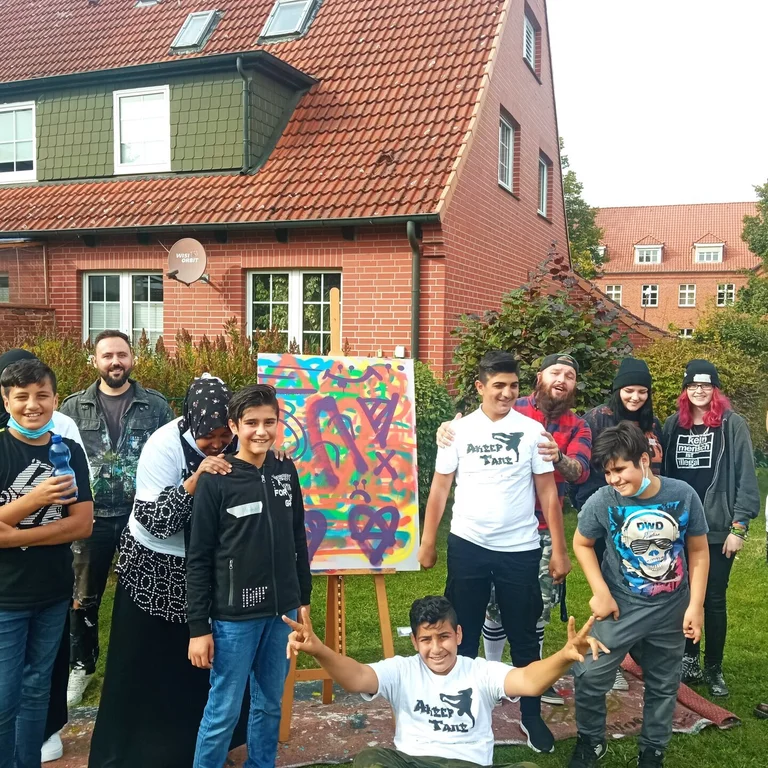 Mehrere Jugendliche und Erwachsene mit Migrationshintergrund stehen vor einem Wohnhaus.