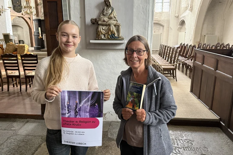 Zwei Frauen stehen mit einem Plakat in einer Kirche.