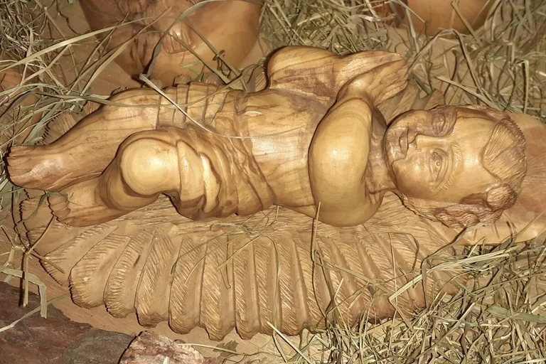 Das aus Holz geschnitzte Christuskind liegt mit betenden Händen in der Krippe