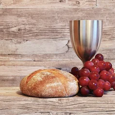 Silberner Kelch, Brot und Weintrauben vor eine Holzwand