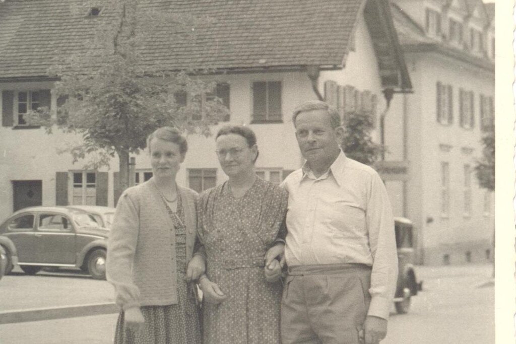 Ein historisches Foto. Drei Menschen sind zu sehen. Sie stehen eingeharkt nebeneinander.