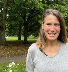 Eine Frau mit langen Haaren steht im Grünen und lächelt in die Kamera.