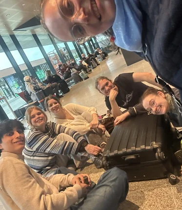 Junge Menschen sitzen mit ihren Koffern auf dem Flughafenboden.