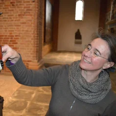 Eine Frau reicht einer kleinen Figur in einer Kirche einen Kugelschreiber.