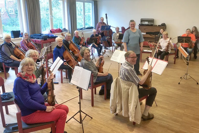 Viele Streicher sitzen auf roten Stühlen und drehen sich nach hinten und schauen in die Kamera