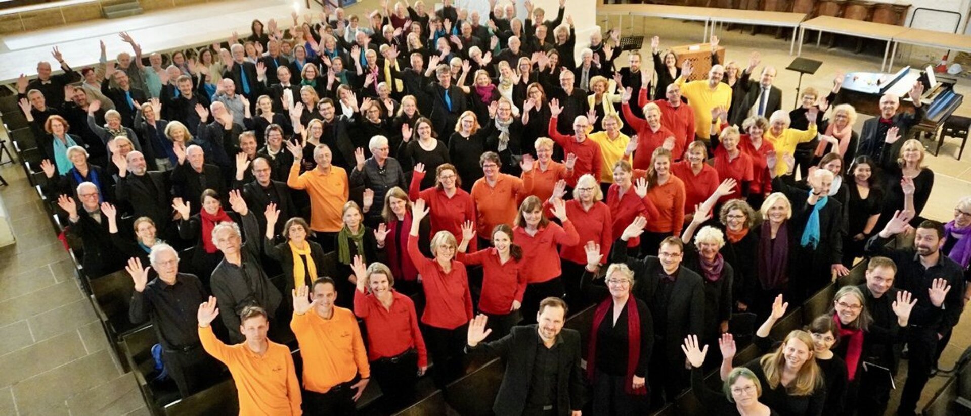 Ein großer Chor in einer Kirche von oben fotografiert winkt in die Kamera.