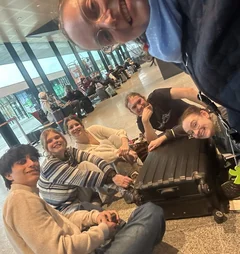 Junge Menschen sitzen mit ihren Koffern auf dem Flughafenboden.