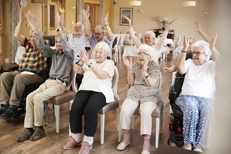 Gruppe von Senioren genießen einen Kurs - Sie lachen, klatschen und halten die Hände hoch. Sie sitzen auf Stühlen
