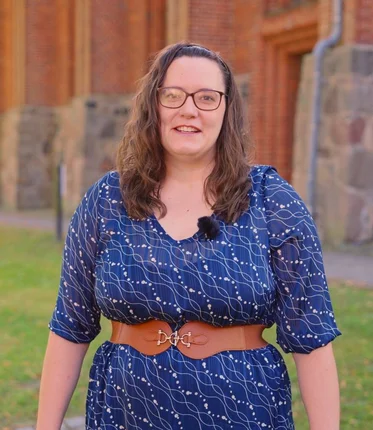 Eine Frau in blauem Kleid steht auf einer Wiese vor einer Kirche.