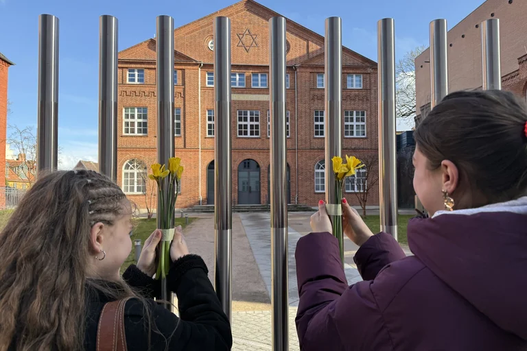 Zwei junge Frauen befestigen Blumen am Zaun einer Synagoge.