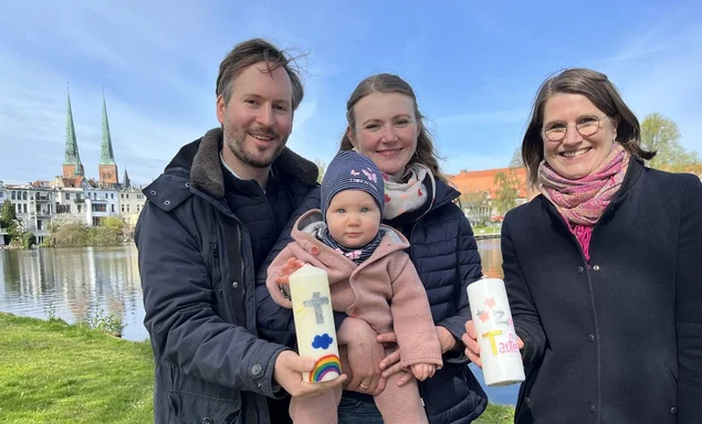 Eine Familie und eine Pastorin stehen vor einem Gewässer