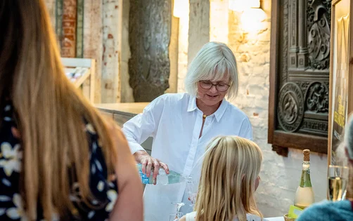 Eine Frau mit weißer Bluse gießt Getränke ein. 
