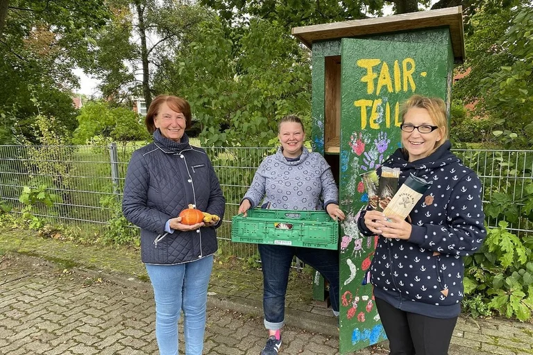 Drei Frauen stehen mit Obst und Konserven vor einem grünen Schrank und lächeln in die Kamera.