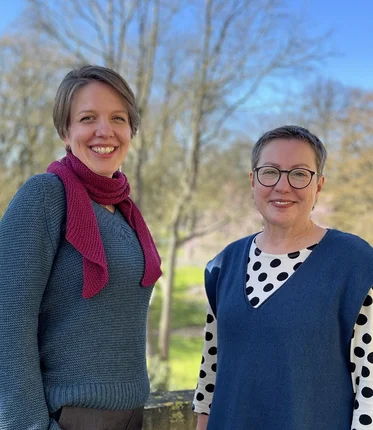 Zwei Frauen stehen im Freien und lächeln in die Kamera.