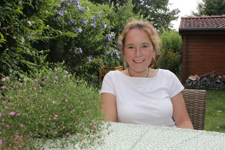 Frau sitzt am Tisch in einem Garten.