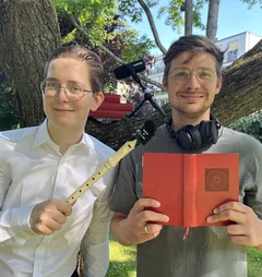 Zwei Männer stehen vor einem Baum und halten eine Blockflöte und ein rotes Gesangbuch.