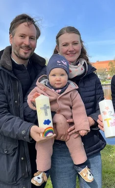 Eine Familie und eine Pastorin stehen vor einem Gewässer
