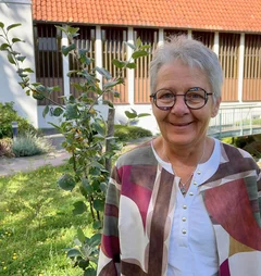 Frau steht vor einem kleinen Apfelbaum und lächelt.