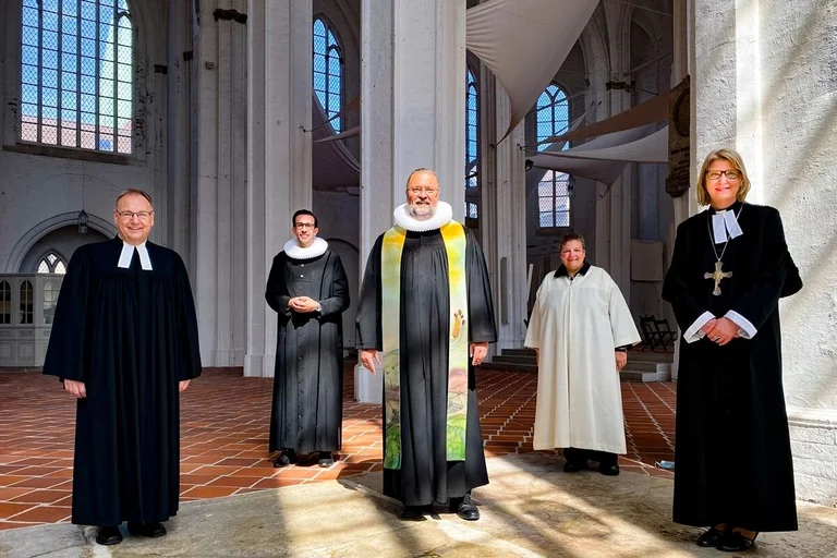 Fünf Pastor:innen, im Hintergrund der Innenraum der Lübecker Petrikirche.