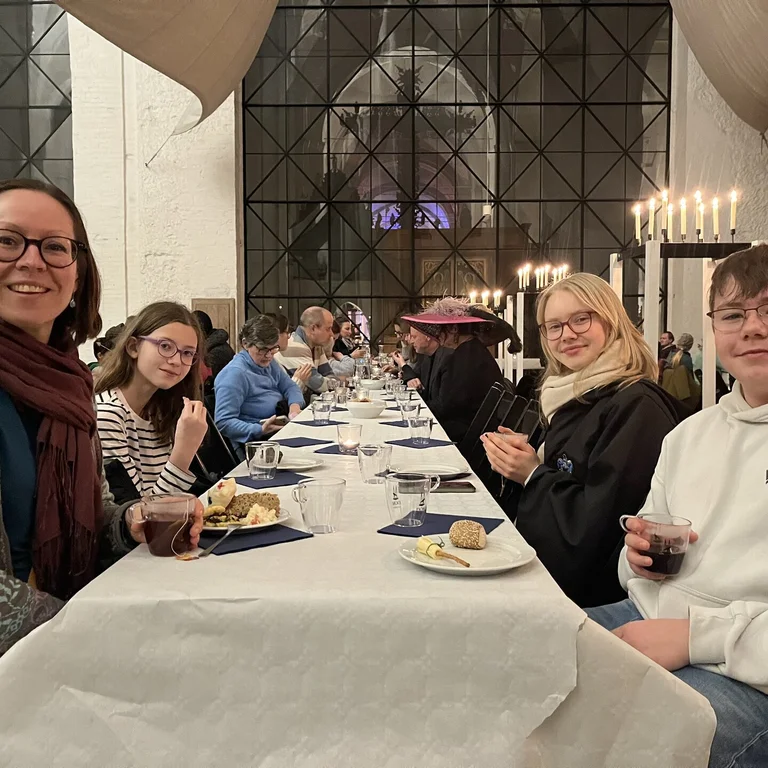 Eine Frau sitzt mit drei Kindern an einem langen Tisch.