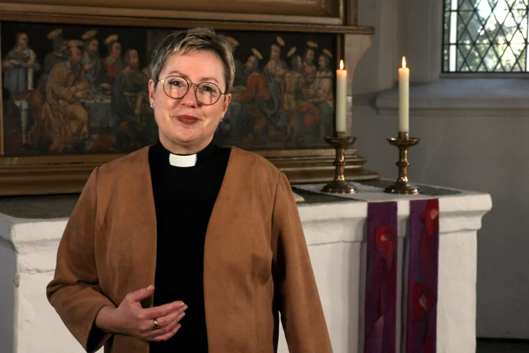Eine Frau steht in einer Kirche und lächelt in die Kamera. 