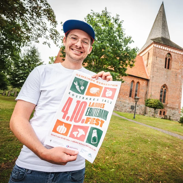 Ein Mann steht mit einem Plakat vor einer Kirche 