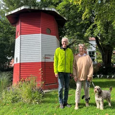 Ein Mann und eine Frau stehen lächelnd vor einem Leuchtturm.