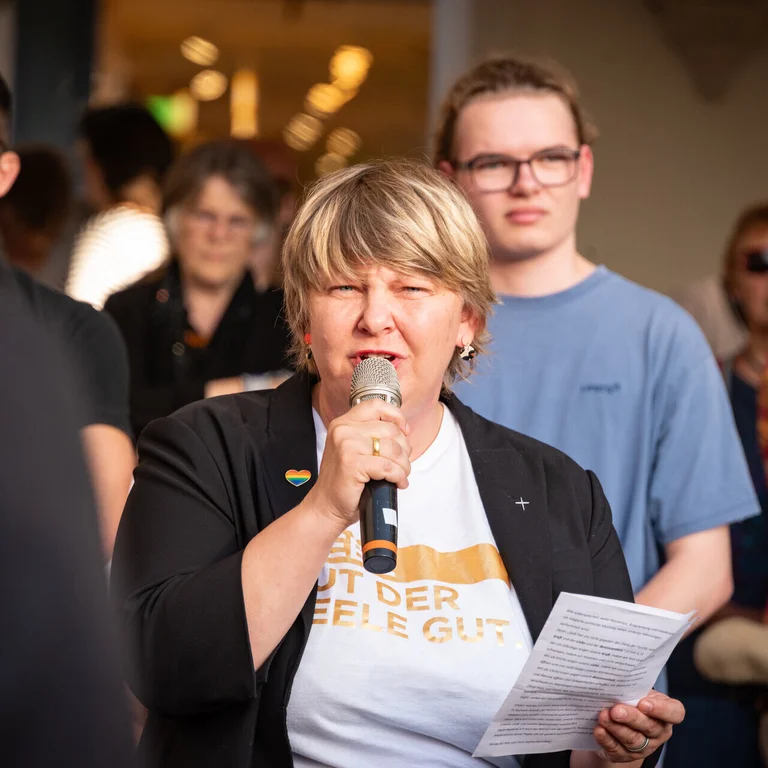Eine Frau mit kurzen blonden Haaren spricht auf einer Demo in ein Mikrofon