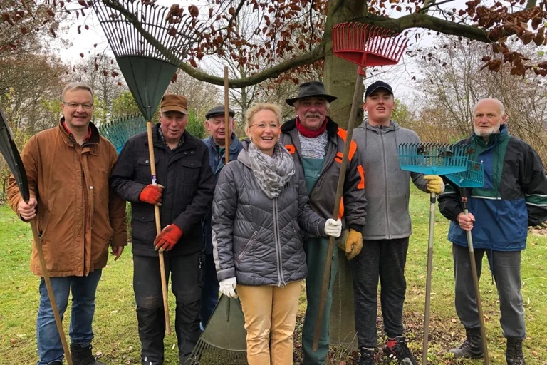 Eine Gruppe von freiwilligen Helfern mit Laubharken unter einem Baum