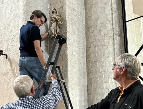 Drei Personen an einem Kirchenpfeiler bei der Anbringung einer Statue.