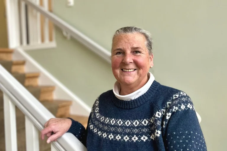 Eine Frau mit grauen zusammengebundenen Haaren und Norweger-Pulli lächelt in die Kamera.