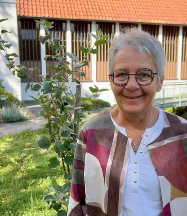 Frau steht vor einem kleinen Apfelbaum und lächelt.
