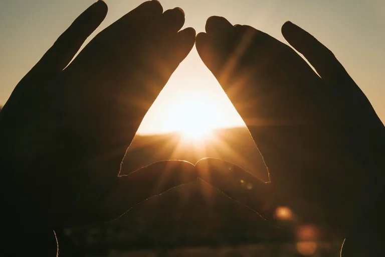 Zwei Hände formen ein Dreieick, durch dass die Sonne scheint.