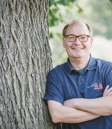 Ein Mann lehnt sich lächelnd an einen Baum.